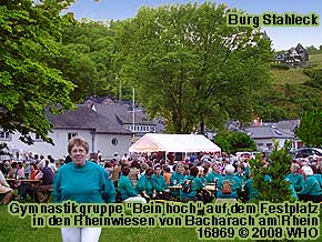 Gymnastikgruppe "Bein hoch" auf dem Festplatz in den Rheinanlagen in Bacharach am Rhein. Rechts oben Burg Stahleck.